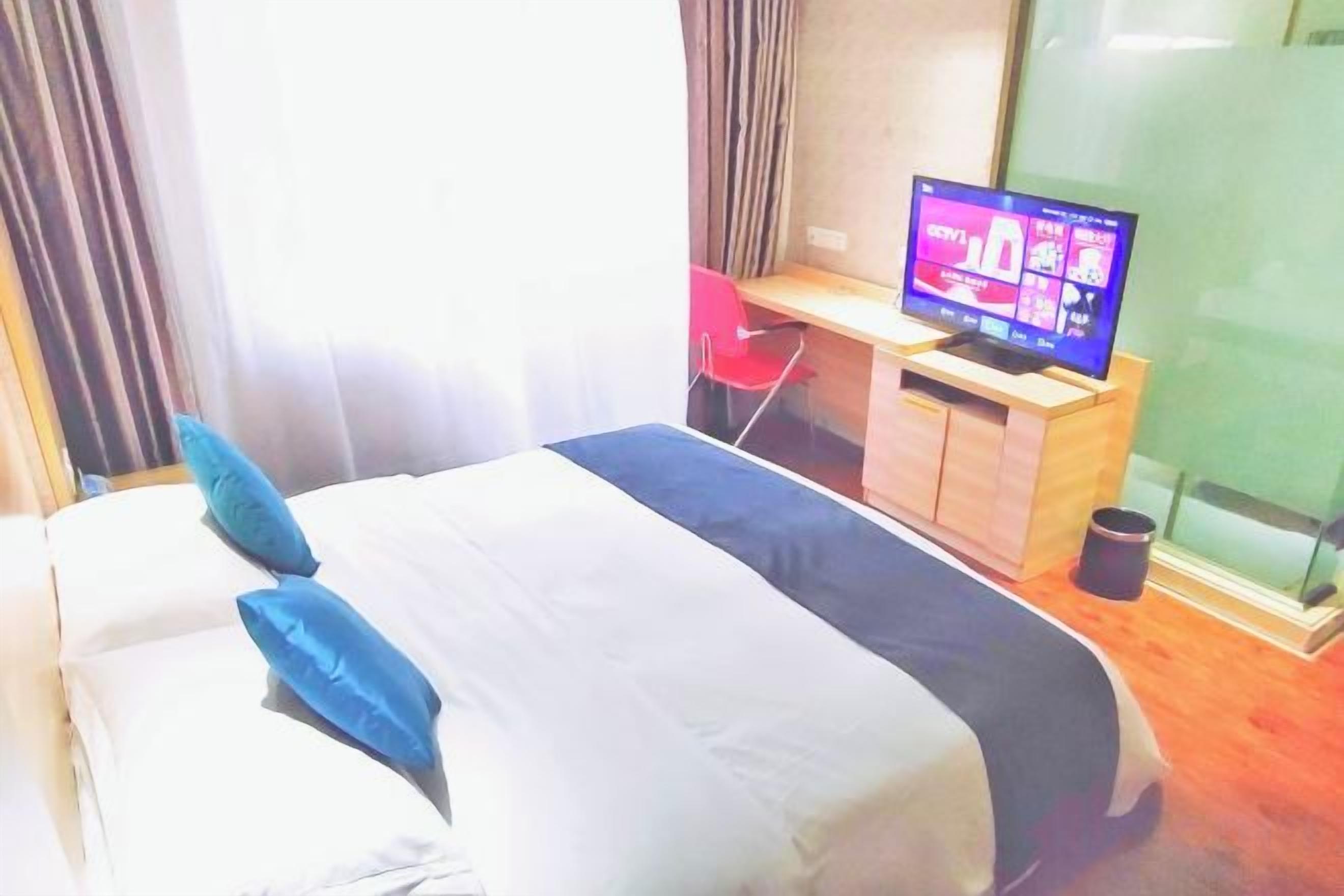 Habitación de hotel con cama, televisor sobre un soporte de madera y escritorio con silla.