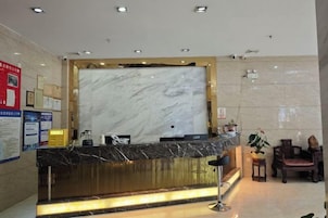 Zona de recepción de un hotel con un mostrador de mármol, un espacio de espera con sillones y un tablón informativo en la pared.