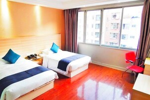 Habitación de hotel con dos camas, una silla roja, un escritorio y un ventanal con vistas a edificios.
