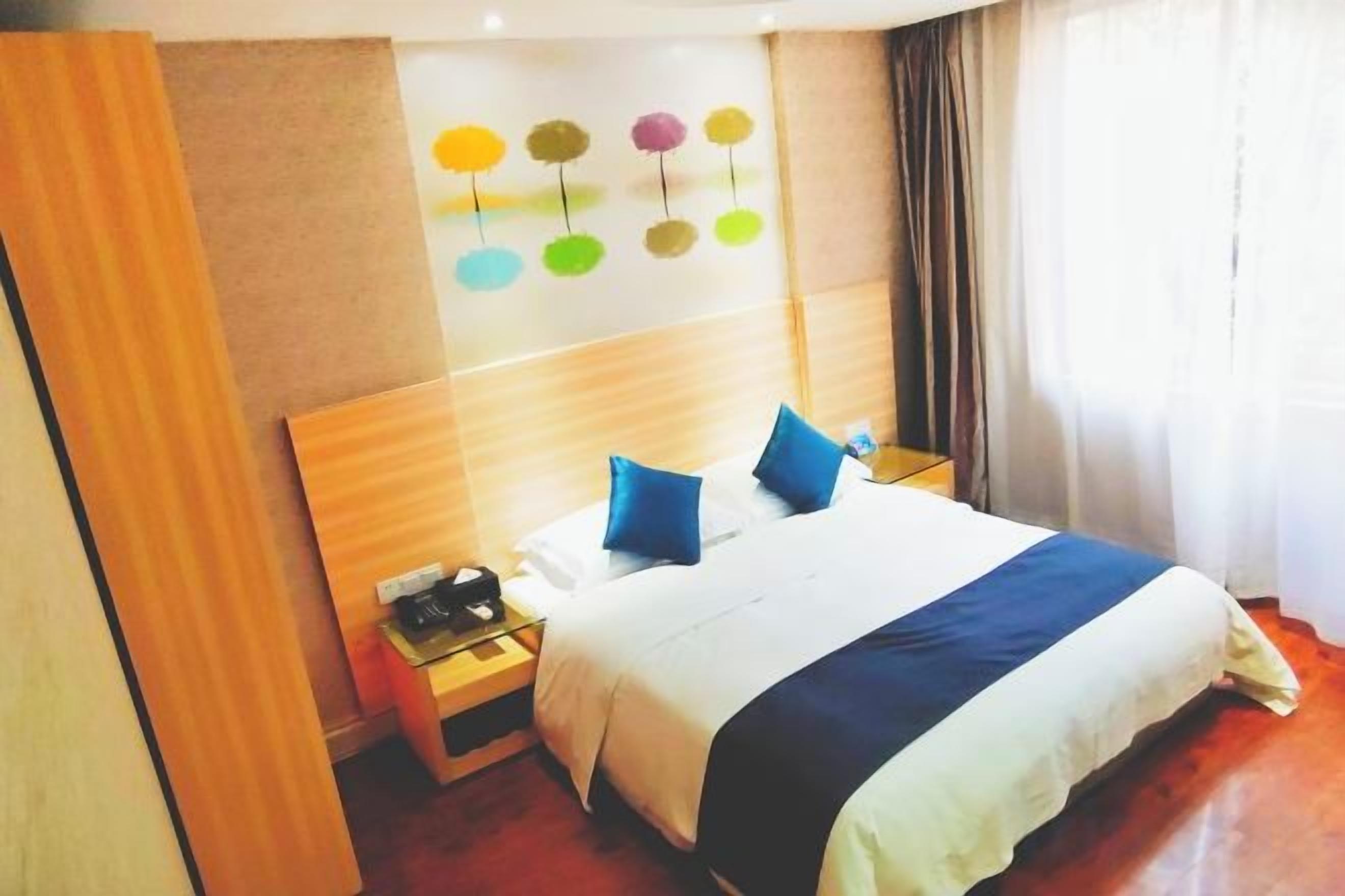 Una habitación de hotel con cama, mesita de noche, una obra de arte en la pared y una ventana con cortinas.