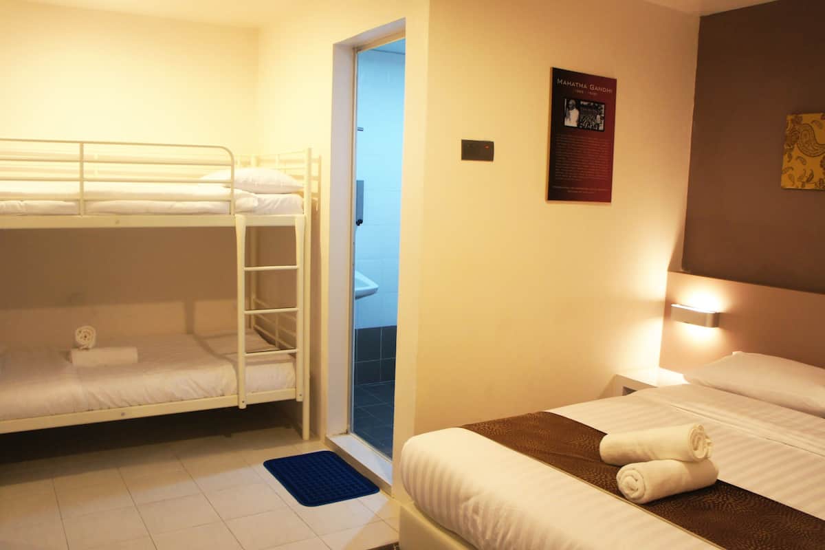 Una habitación de hotel con literas, una cama individual, una mesita de noche y un cartel en la pared.