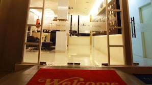 A hotel entrance with a red 'Welcome' mat, a reception desk, and a view into the lobby area. - DWJ Hotel (Ipoh)