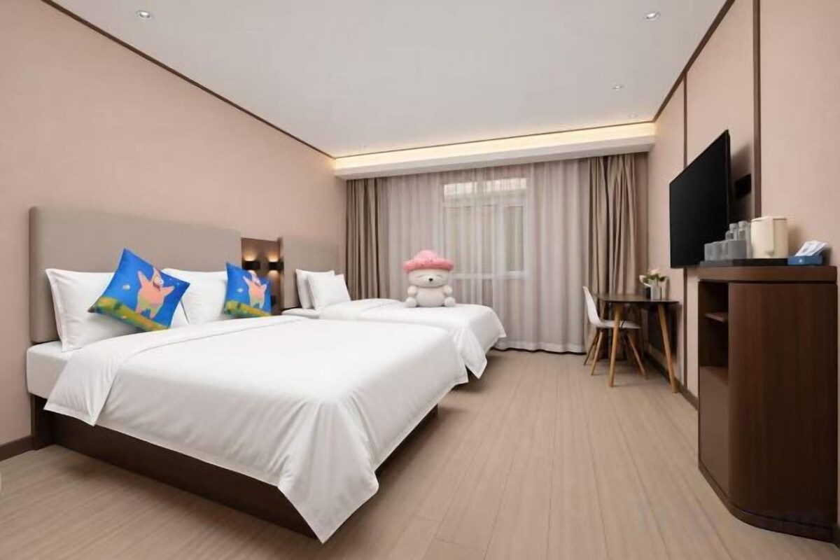 Habitación de hotel con dos camas, un escritorio, una silla, un televisor y un ventanal con cortinas.