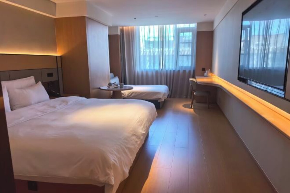 A hotel room with two beds, a desk, a chair, a TV, and a window with curtains.