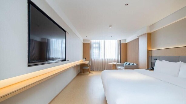 A modern hotel room with a large bed, a desk, a chair, and a TV mounted on the wall. - Ji Hotel (Hangzhou)