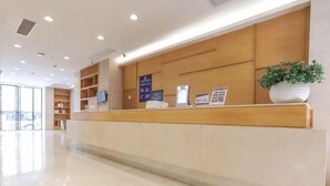 A reception desk with a wooden finish, a potted plant, and informational signs. - Ji Hotel (Hangzhou)