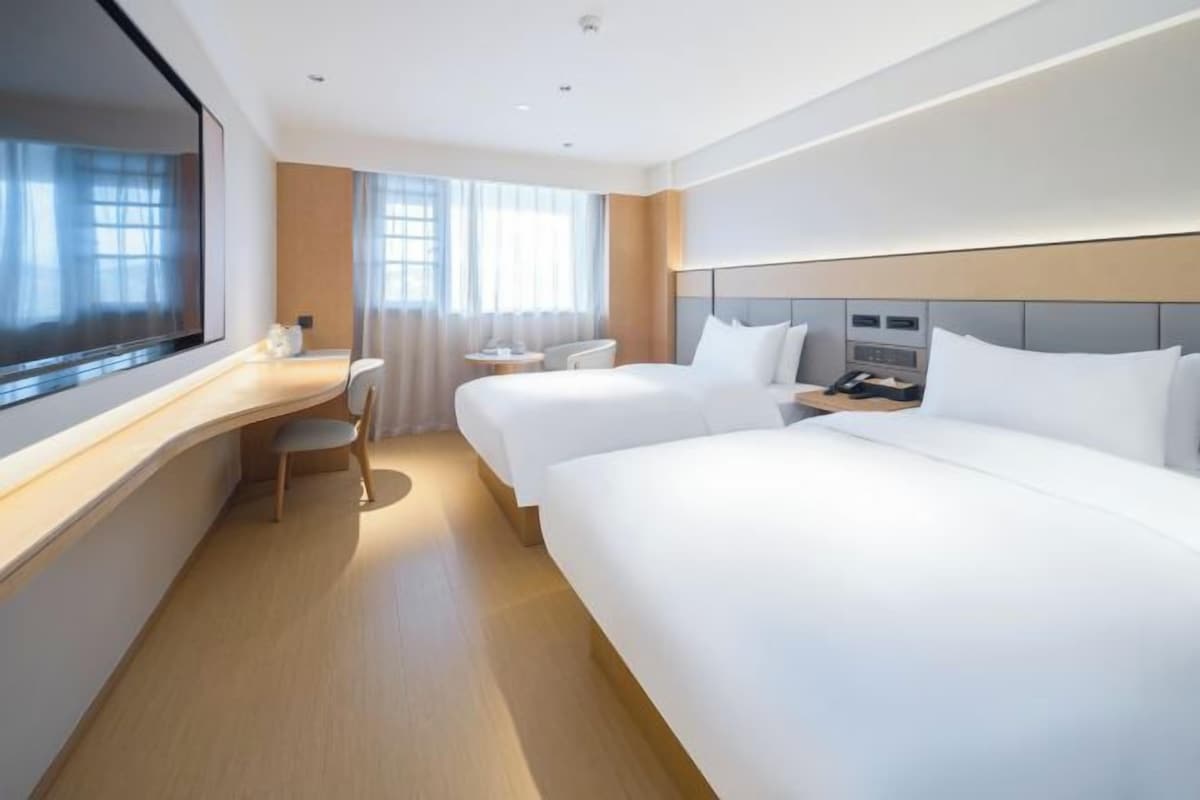 Habitación de hotel con dos camas, un escritorio, una silla y un ventanal grande.