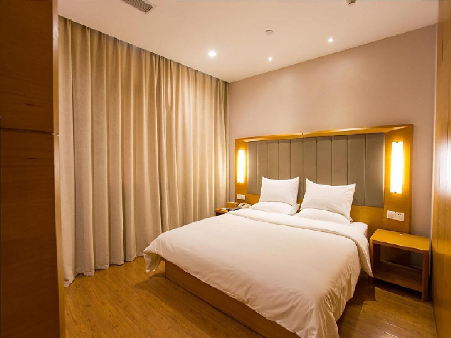 A hotel room with a large bed, wooden headboard, bedside tables, and a curtain.