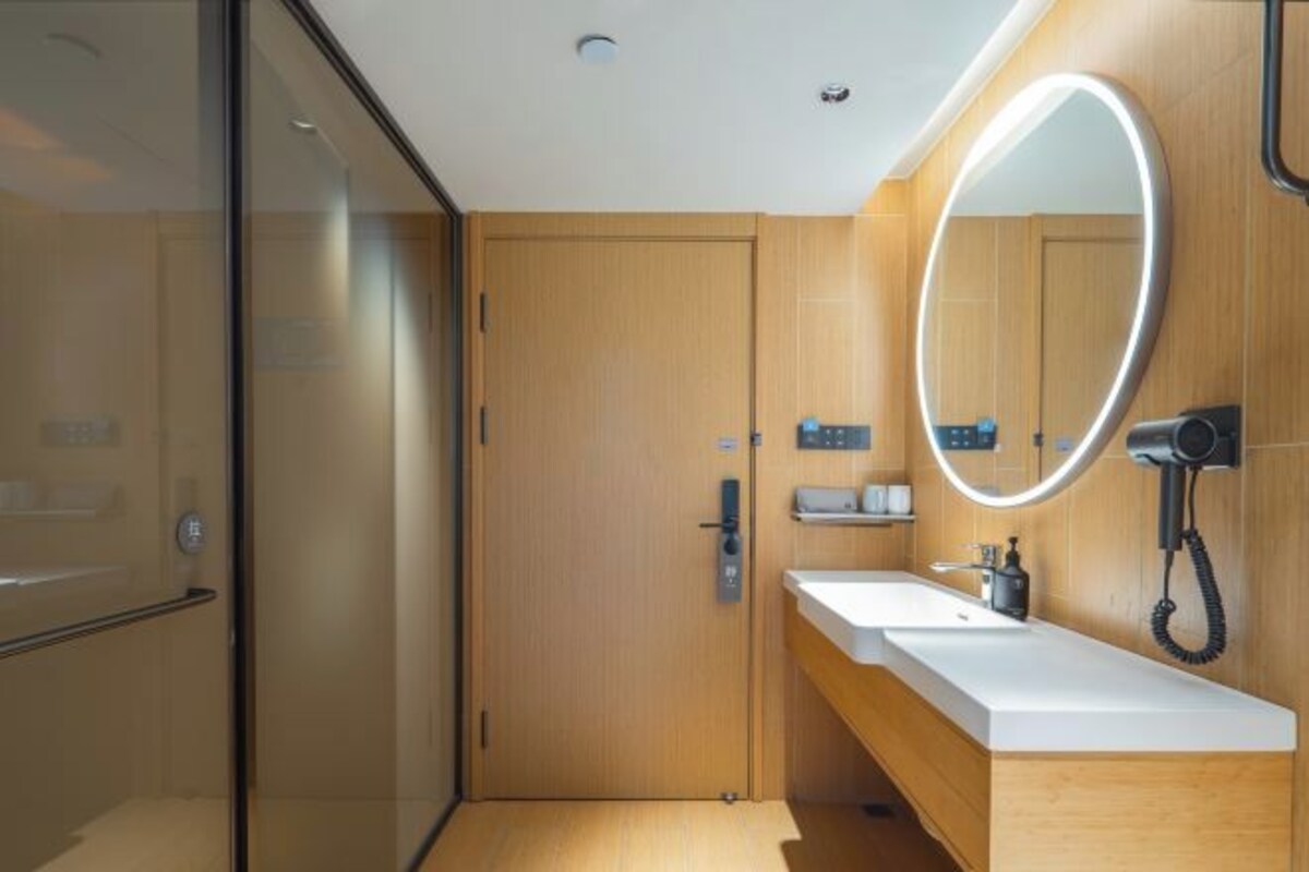 A modern bathroom with a wooden vanity, a large mirror with a light, and a hairdryer on the wall.