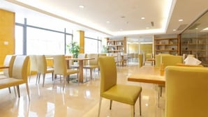 A modern library with yellow chairs and tables, large windows, and bookshelves. - Ji Hotel (Hangzhou)