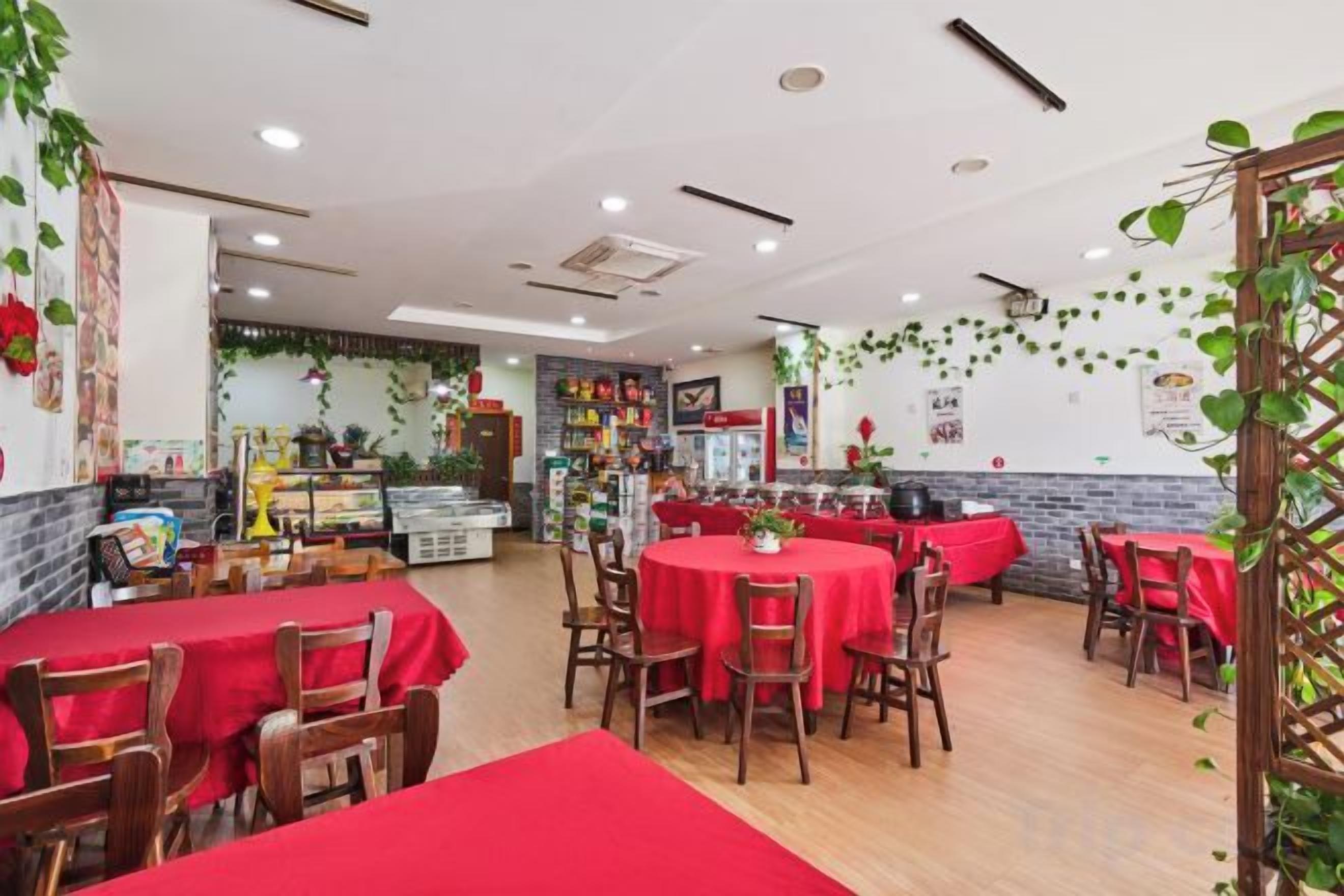 A restaurant with round tables, red tablecloths, and wooden chairs.