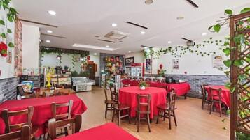 A restaurant with round tables, red tablecloths, and wooden chairs.