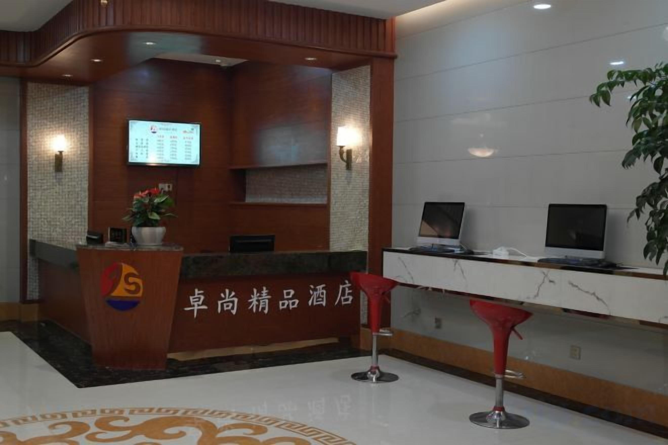A hotel reception area with a reception desk, a digital screen, and a plant.