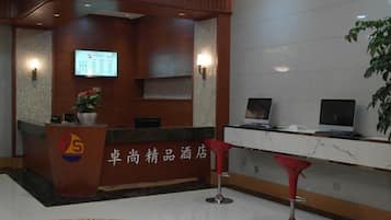 A hotel reception area with a reception desk, a digital screen, and a plant.