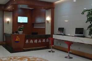 Zona de recepción de un hotel con mostrador, pantalla digital y una planta.