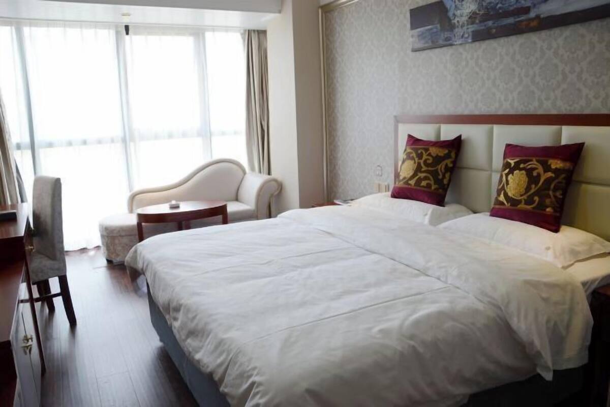 A hotel room with a large bed, a sitting area with a chair and a small table, and a large window providing a view.