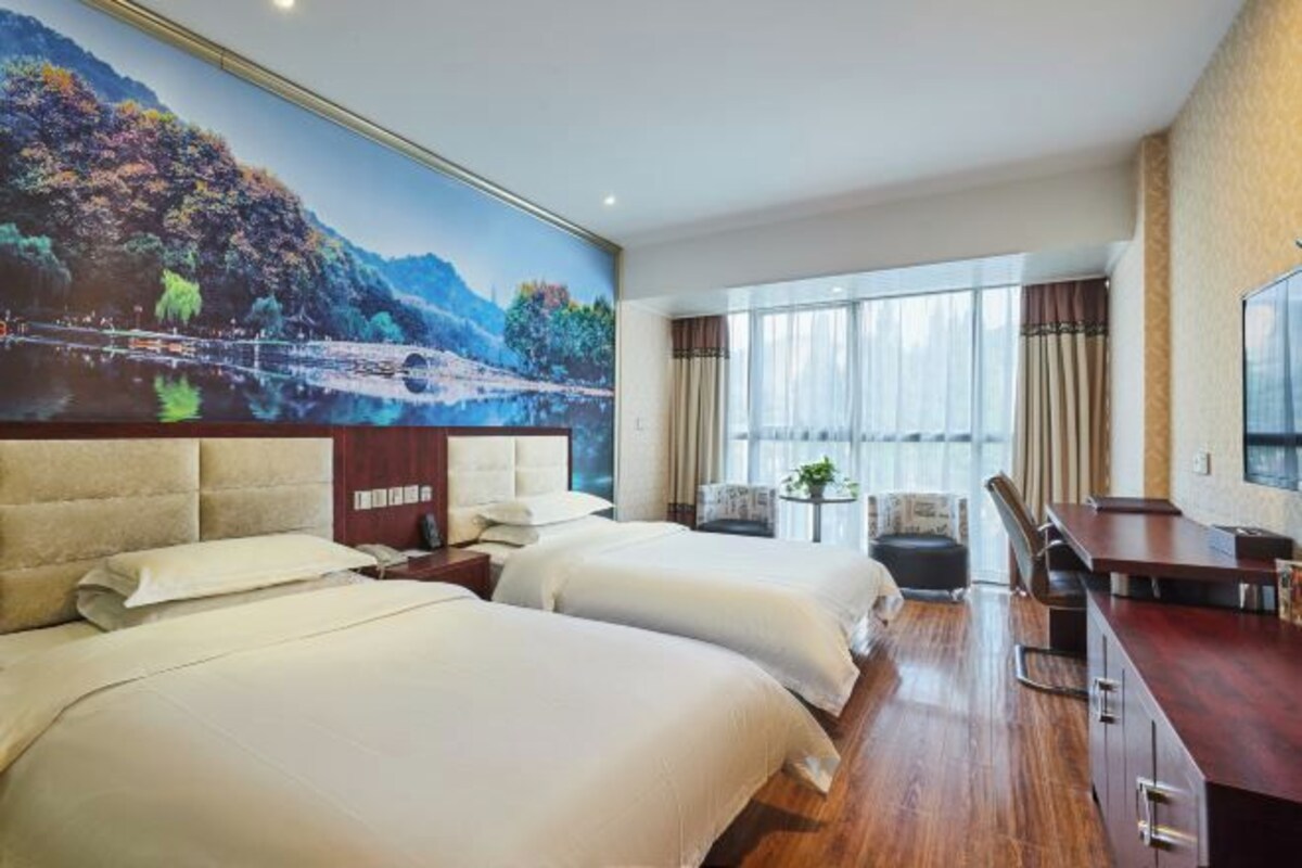 Quarto de hotel com duas camas, uma mesa de jantar e uma janela grande com cortinas.