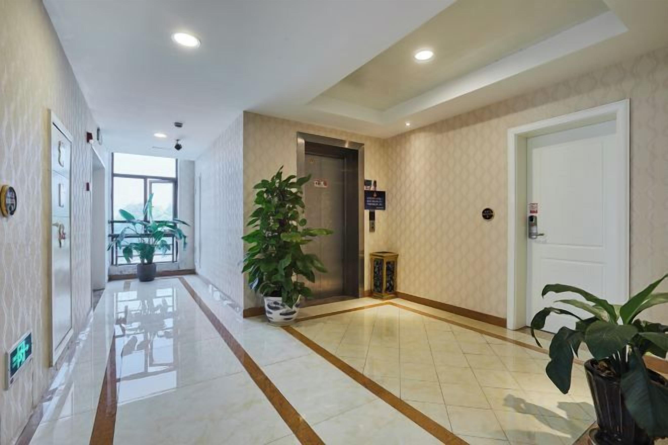 Corredor de hotel com piso de azulejos brilhantes, planta em vaso, porta e elevador.