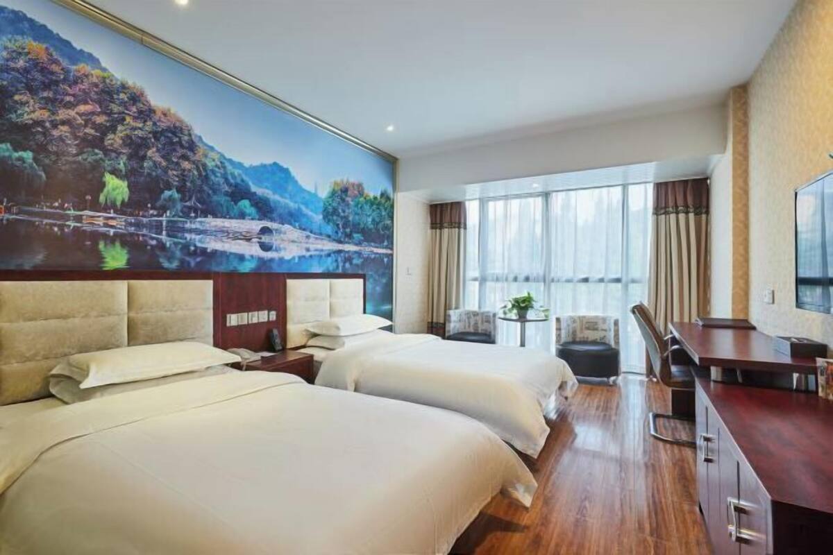 A hotel room with two beds, a dining table, and a large window with curtains.