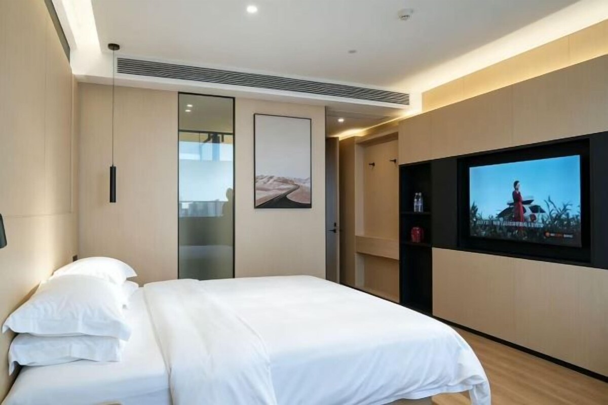 Ett modernt hotellrum med en säng, en tv och ett stort fönster.