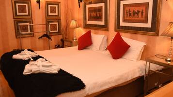 A neatly made bed with white and red pillows, a black throw blanket, and white towels on a wooden floor.