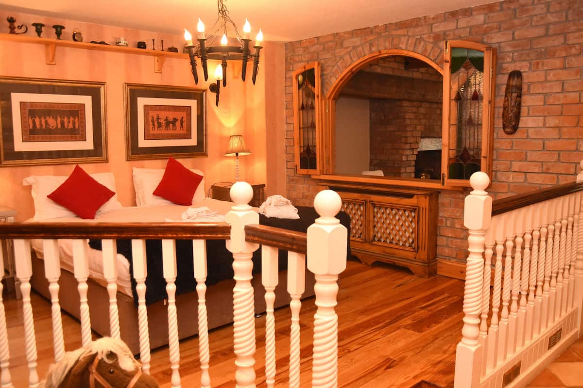 A room with a wooden bed, white railings, a chandelier, framed pictures, and a brick wall.