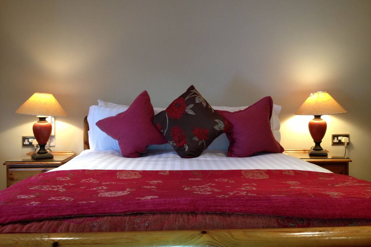 A neatly made bed with a red bedspread and two decorative pillows, flanked by two bedside lamps.