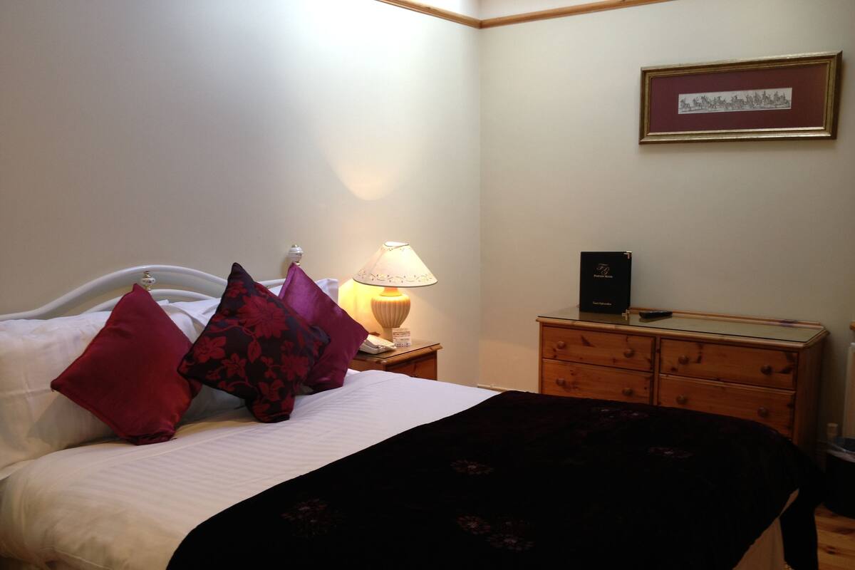 A neatly made bed with a white headboard, a lamp, a framed picture on the wall, and a wooden dresser.