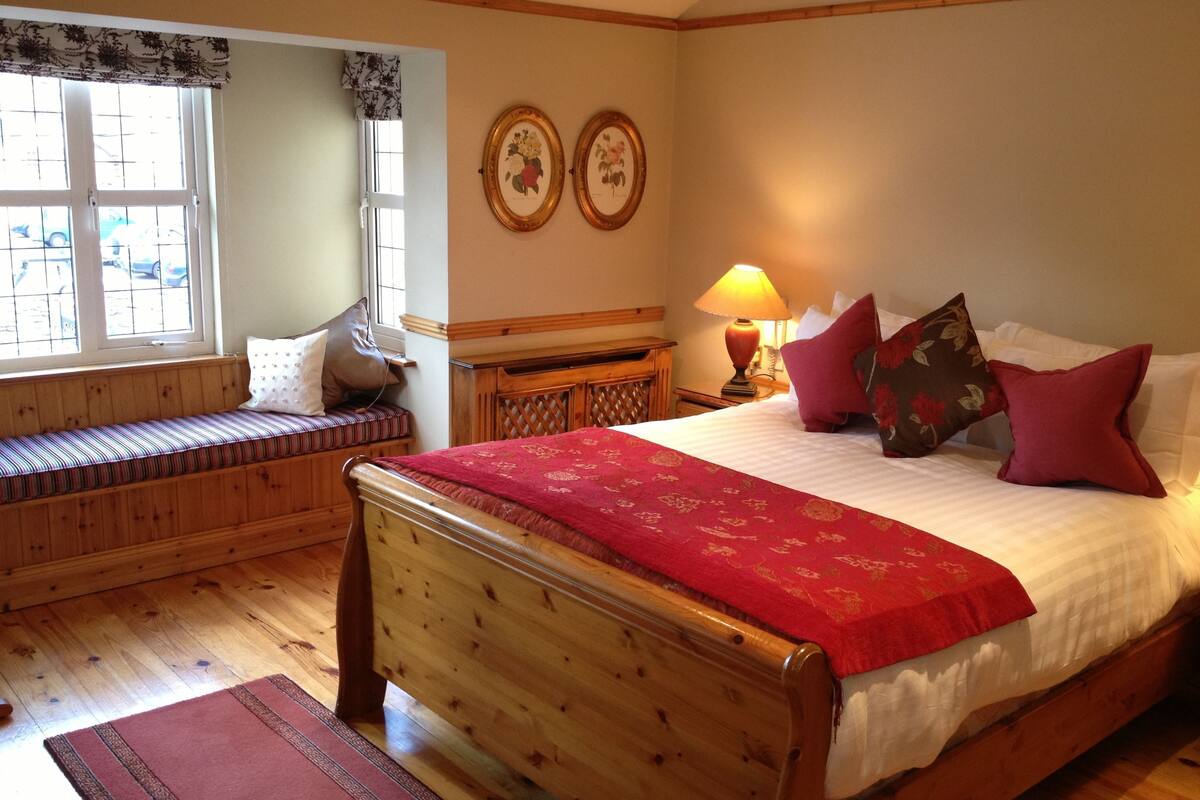 A wooden bed with a red bedspread, a bench with cushions, a nightstand with a lamp, and two framed pictures on the wall.