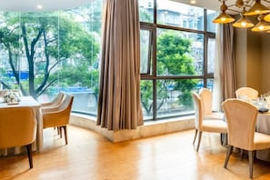 A dining area with a table and chairs, large windows, and a view of trees and buildings. - Yunnan Weiju Golden Eagle Grand Hotel (Kunming Railway Station Shuangqiao Night Market Style Street) (Kunming)