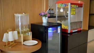 A kitchen area with a refrigerator, a popcorn machine, a water dispenser, and a small table with a plate and cups.