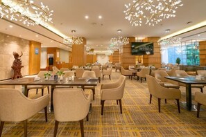 A hotel dining area with multiple tables and chairs, a patterned carpet, and a television screen on the wall. - Yunnan Weiju Golden Eagle Grand Hotel (Kunming Railway Station Shuangqiao Night Market Style Street) (Kunming)