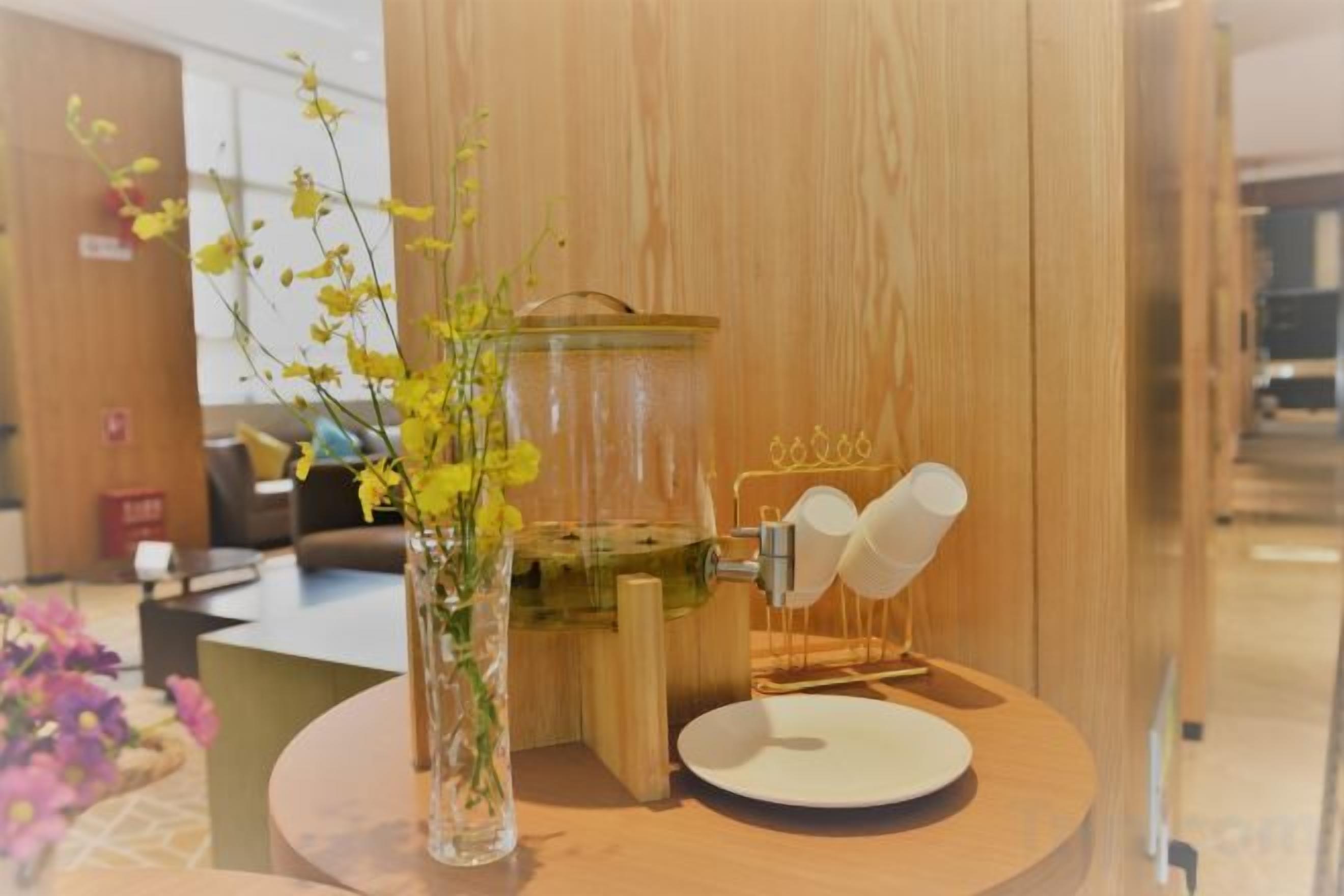 Una cafetera, un florero con flores y un plato blanco sobre una mesa de madera.
