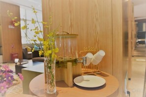 A coffee machine, a glass vase with flowers, and a white plate on a wooden table. - Yunnan Weiju Golden Eagle Grand Hotel (Kunming Railway Station Shuangqiao Night Market Style Street) (Kunming)