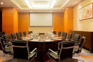 A conference room with a large oval table, black chairs, and a projector screen.
