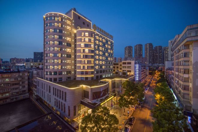 A multi-story hotel with a curved facade, multiple balconies, and a well-lit street in the foreground.