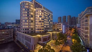 A multi-story hotel with a curved facade, multiple balconies, and a well-lit street in the foreground.