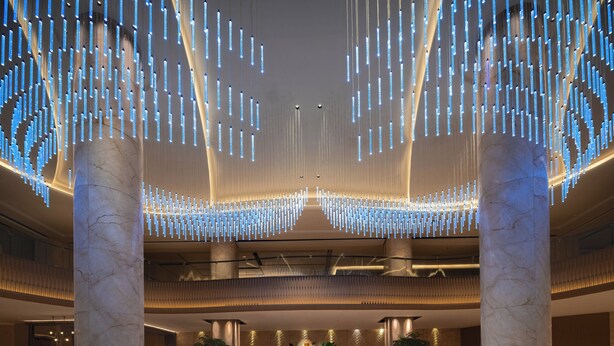 Um hall de entrada com colunas de mármore, balcão de recepção, área de estar e luminárias pendentes.