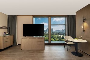 Ein modernes Hotelzimmer mit großem Fenster, Flachbildfernseher, Esstisch und einer Sitzecke.