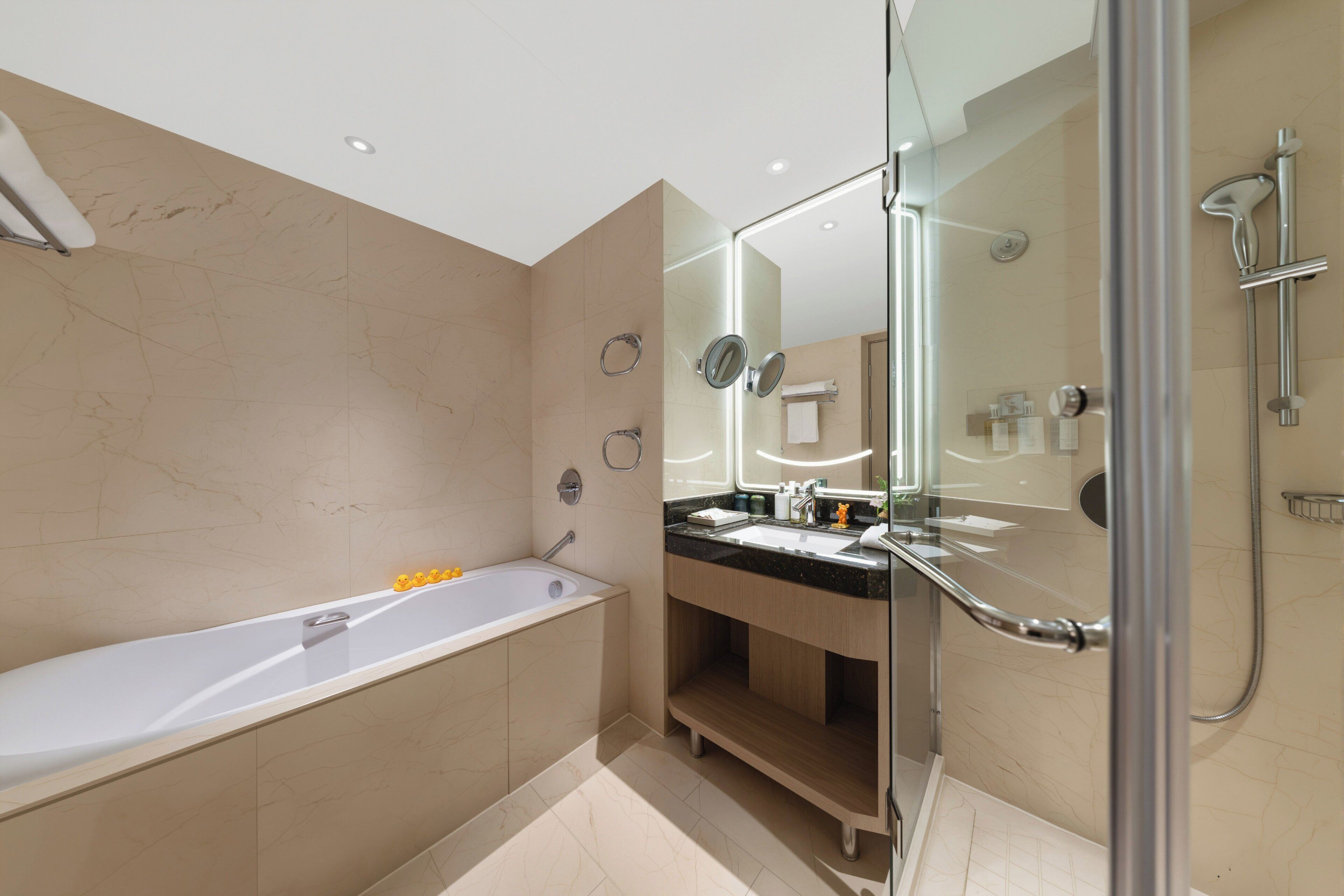 Un baño moderno con bañera, ducha con mampara de vidrio y tocador con espejo.