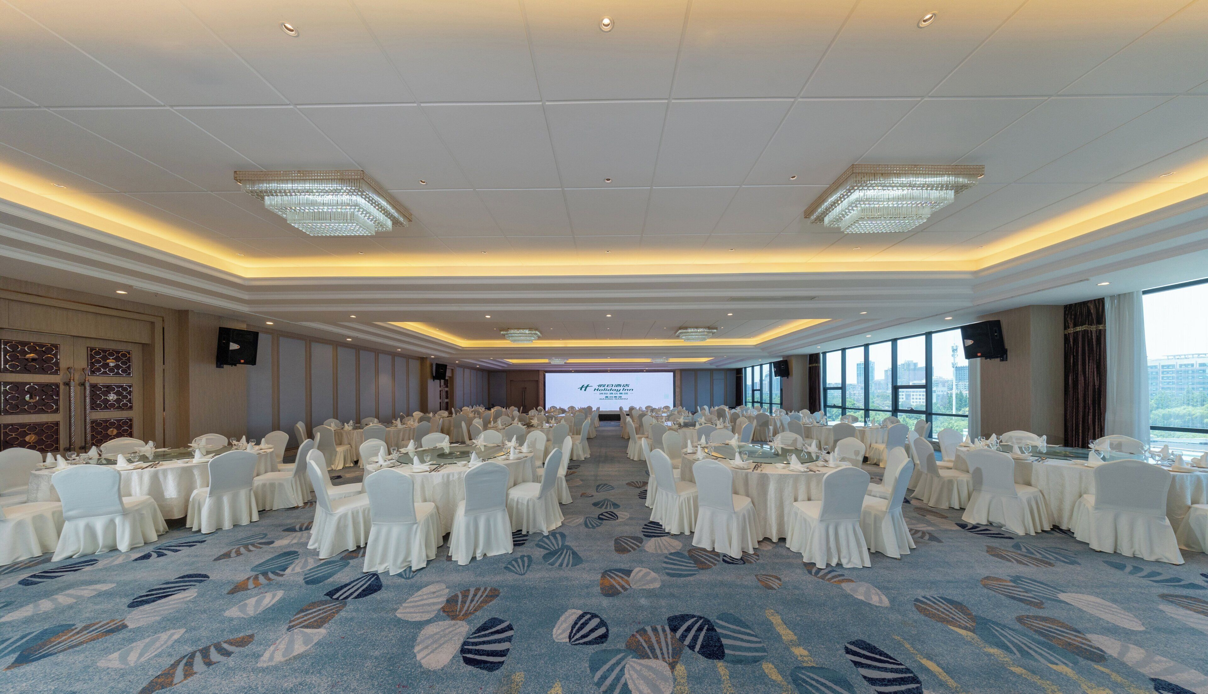 A large conference room with rows of tables and chairs, a projector screen, and large windows.