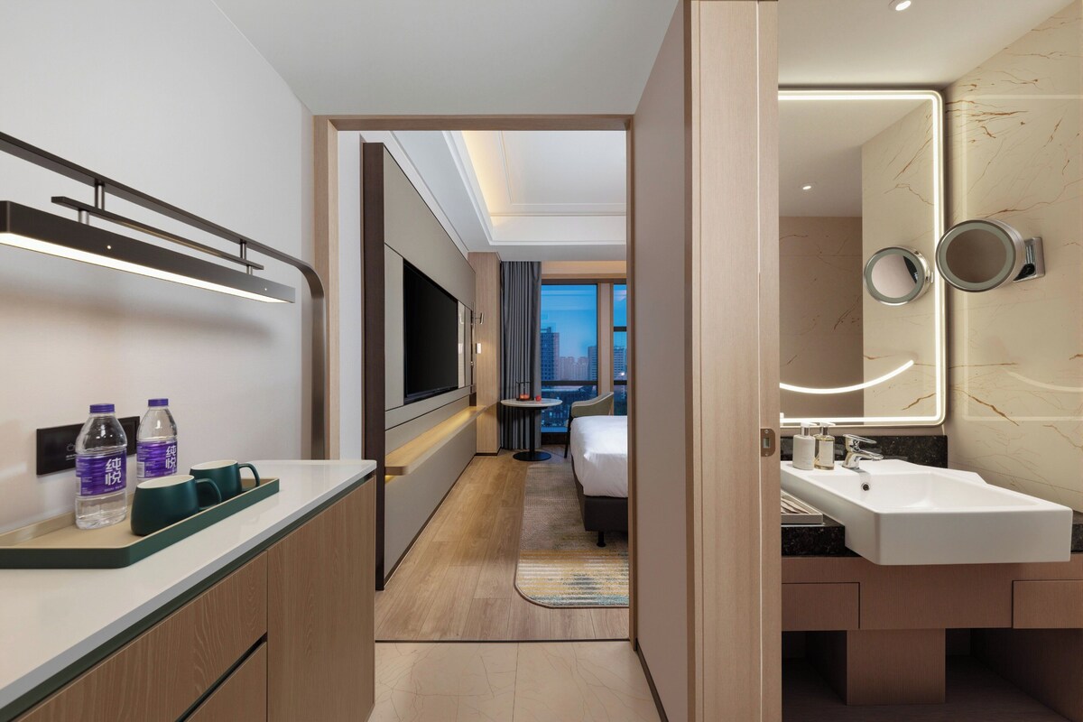 Habitación de hotel moderna con televisión, minibar y vistas a la ciudad.