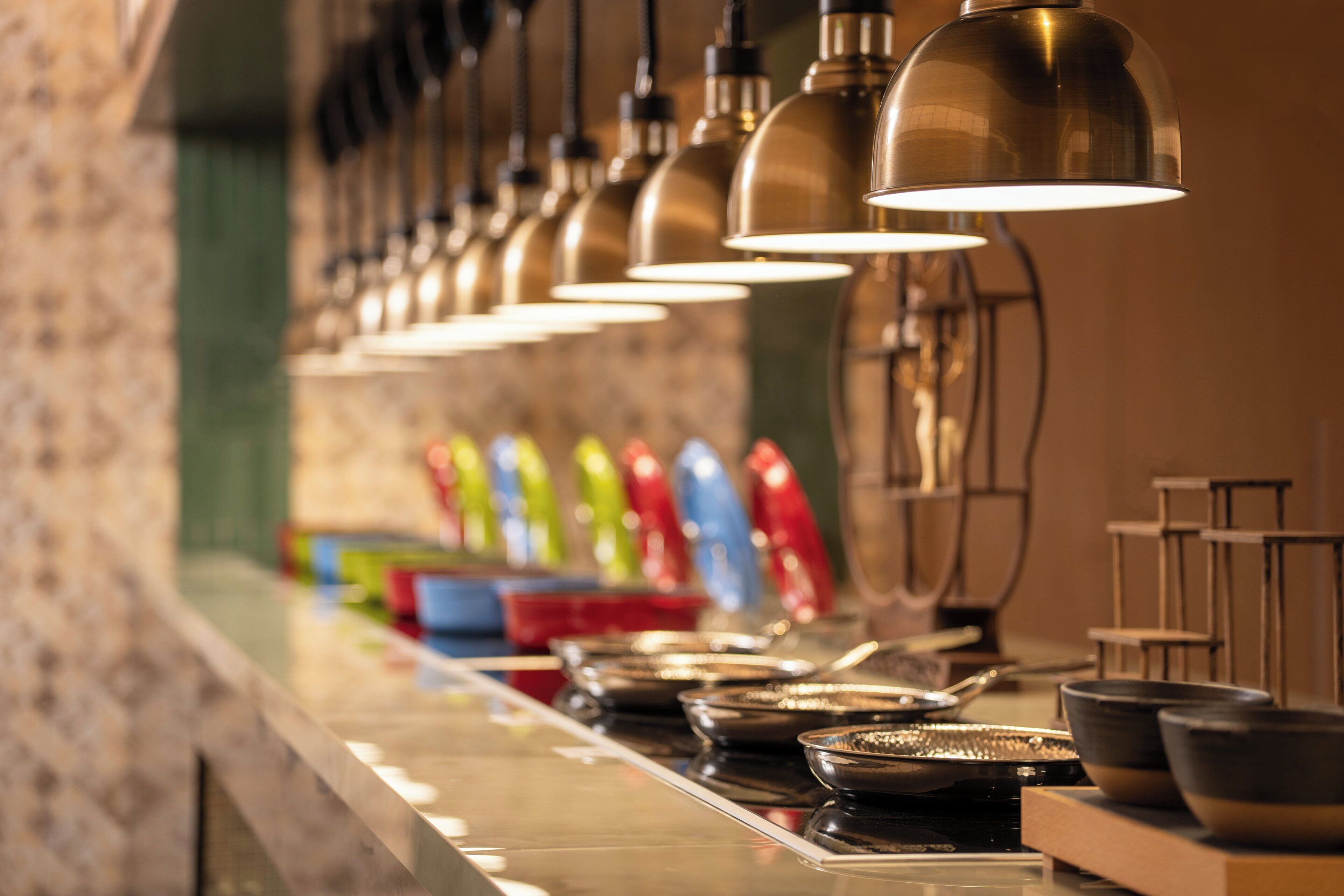 A row of metal bowls and plates on a counter with overhead lighting.