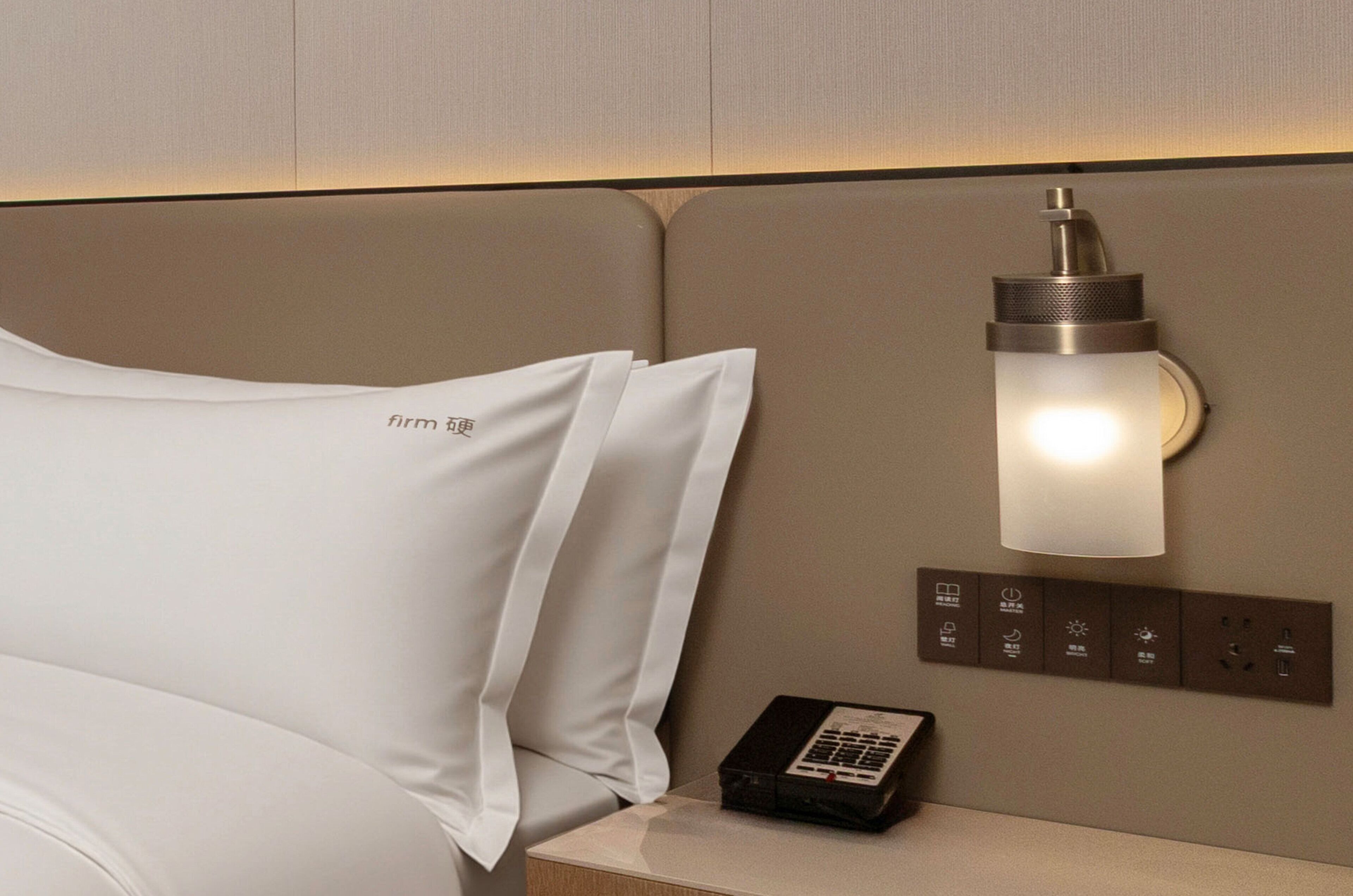 Una camera d'albergo con un letto, un comodino con una lampada e un pannello di controllo con diversi pulsanti.