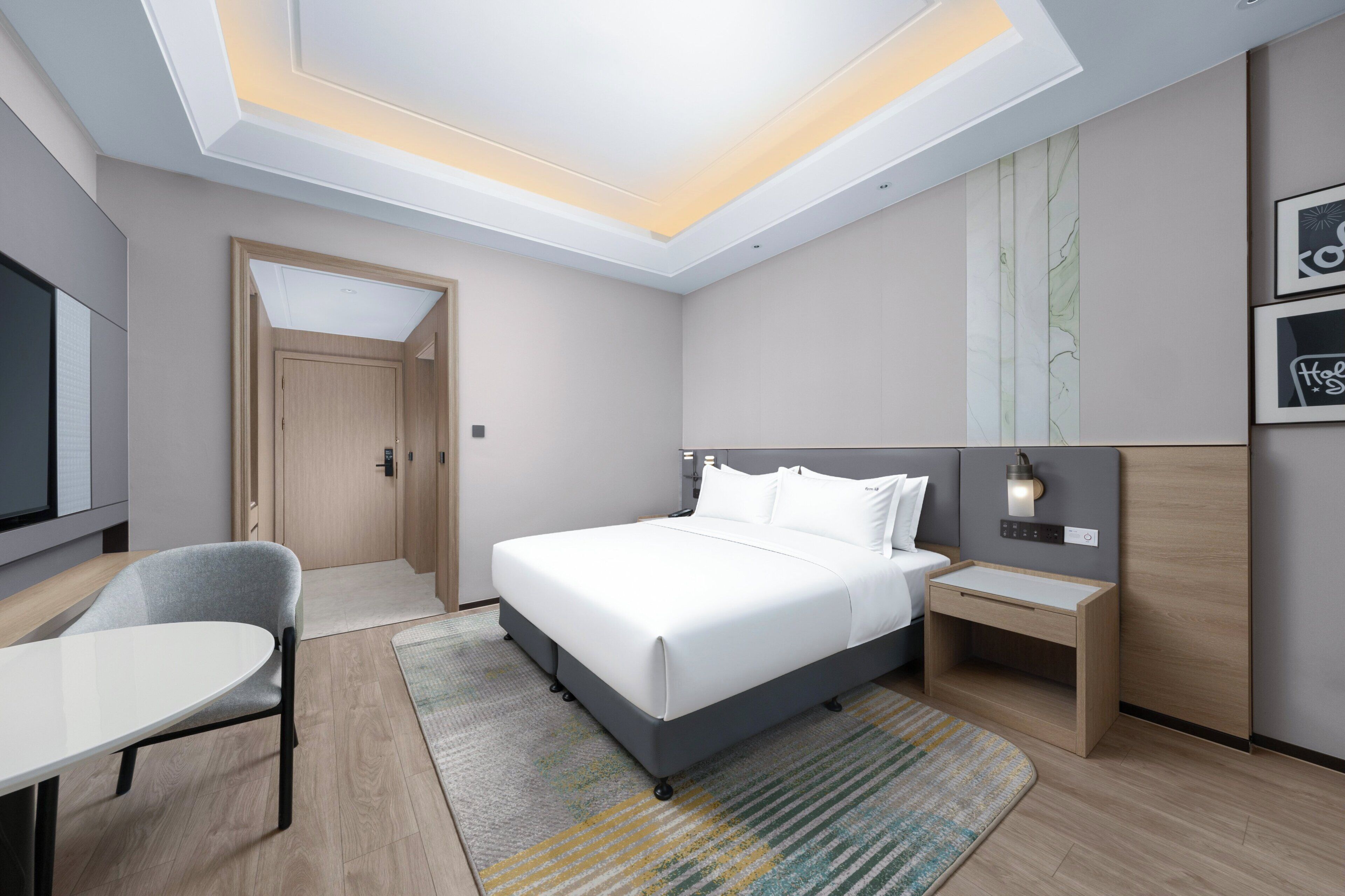 A modern hotel room with a bed, bedside table, chair, and a desk.