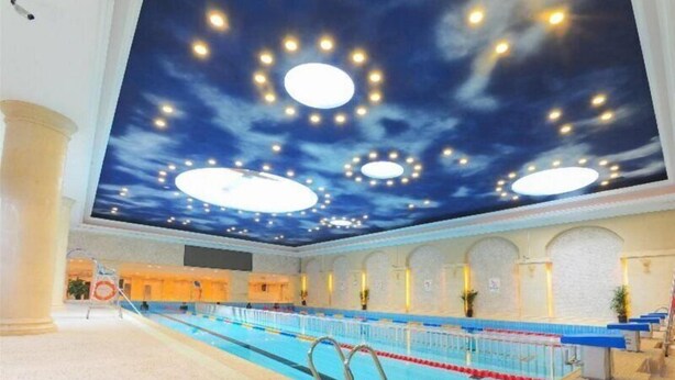 A swimming pool with a ceiling that has a sky and cloud design, and multiple circular light fixtures.