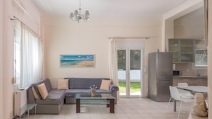 A living room with a sofa, a glass coffee table, and a painting of a beach. - Villas F & B Summer Collection - Aegean Residence (Kassandra)