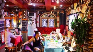 A restaurant with wooden beams and a red ceiling, tables with blue tablecloths, and a variety of bottles on the walls. - Leo Hostel (Beijing)