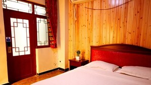 A hotel room with a wooden paneled wall, a bed with white linens, a small bedside table with a plant, and a window with a curtain. - Leo Hostel (Beijing)