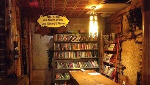 A cozy, dimly lit room with a wooden table and benches, surrounded by shelves filled with books and DVDs. A sign above the shelves reads "Leo Movie World, Leo Library & Games." - Leo Hostel (Beijing)